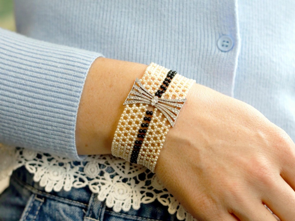 An Art Deco multi-strand pearl and black onyx cuff bracelet featuring a central geometric bow-shaped platinum mount set with diamonds. View V