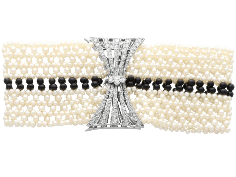 An Art Deco multi-strand pearl and black onyx cuff bracelet featuring a central geometric bow-shaped platinum mount set with diamonds. View VIII