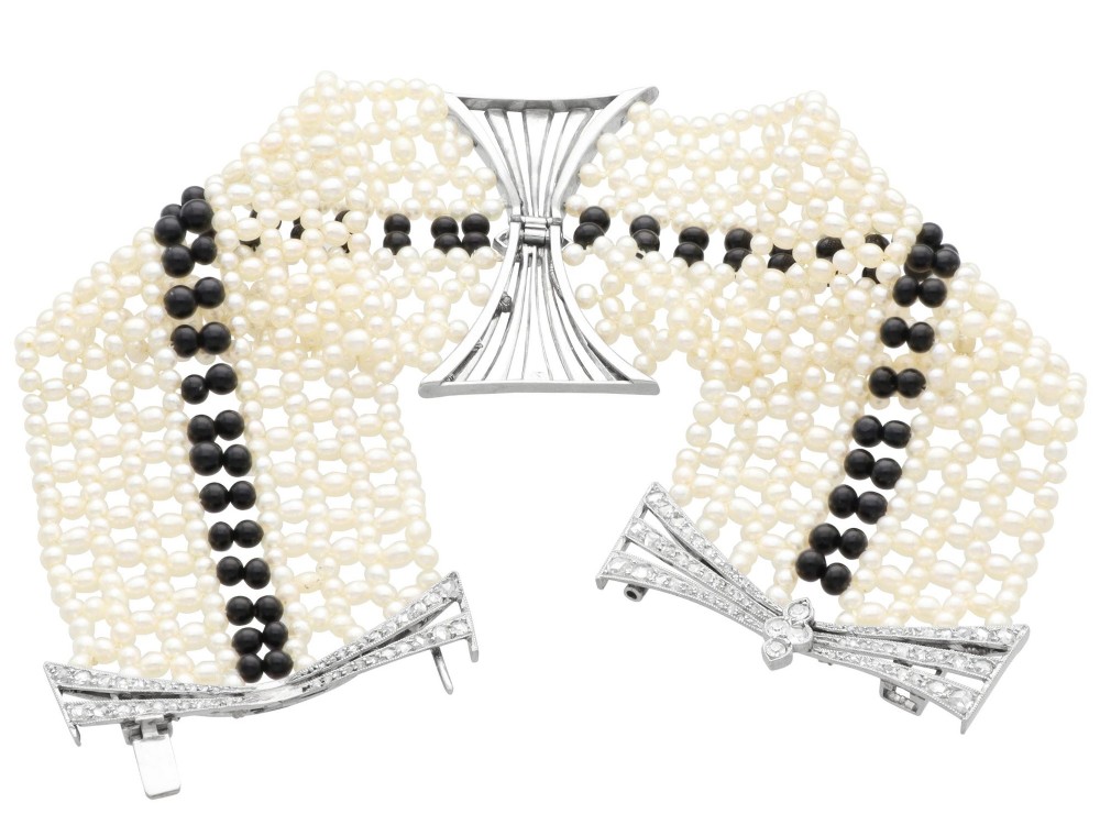 An Art Deco multi-strand pearl and black onyx cuff bracelet featuring a central geometric bow-shaped platinum mount set with diamonds. View IX