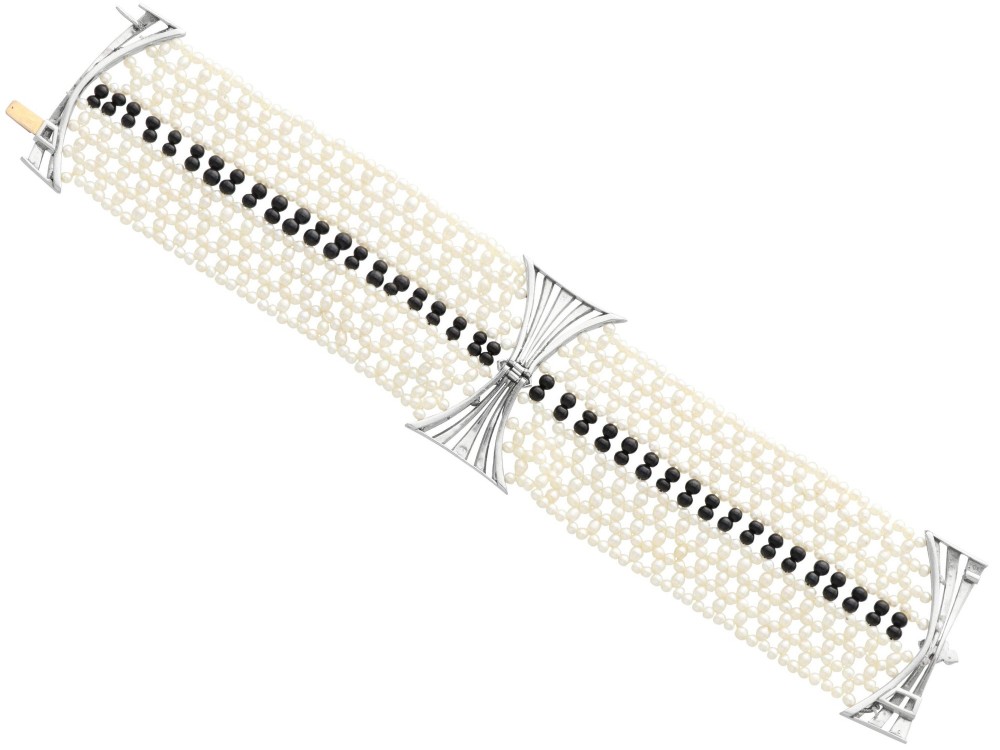 An Art Deco multi-strand pearl and black onyx cuff bracelet featuring a central geometric bow-shaped platinum mount set with diamonds. View XI