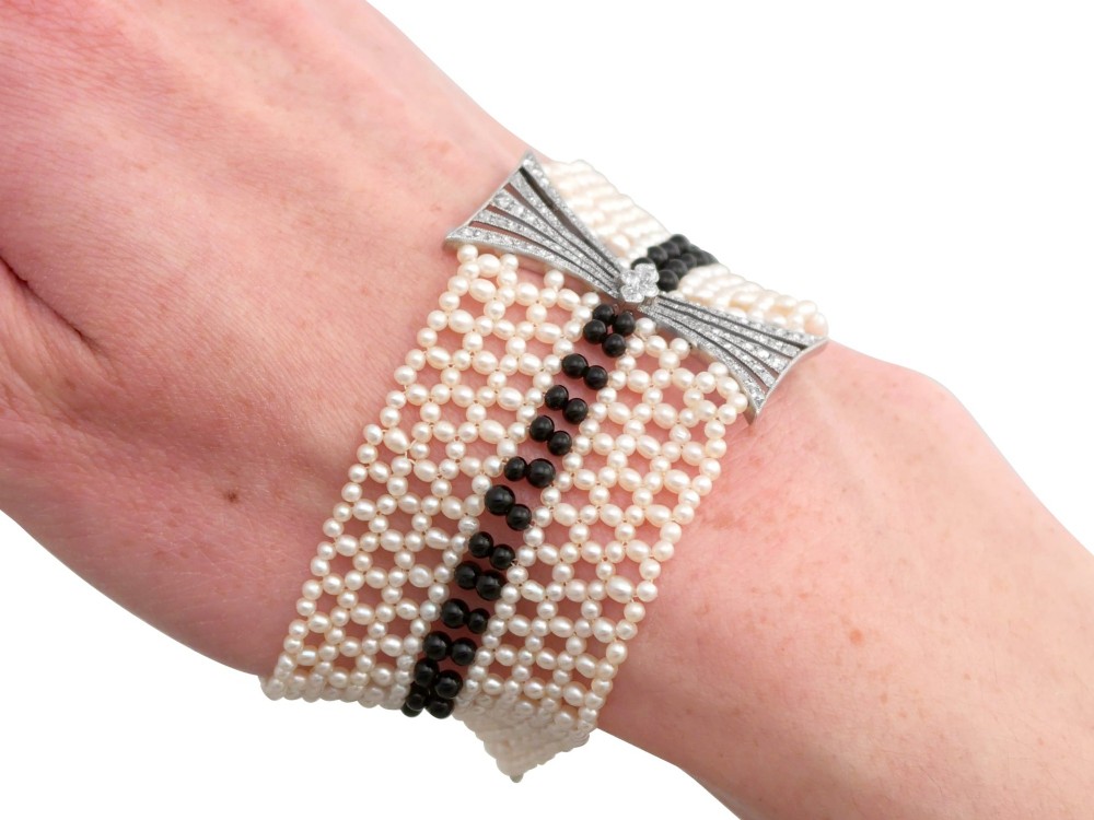 An Art Deco multi-strand pearl and black onyx cuff bracelet featuring a central geometric bow-shaped platinum mount set with diamonds. View XIV