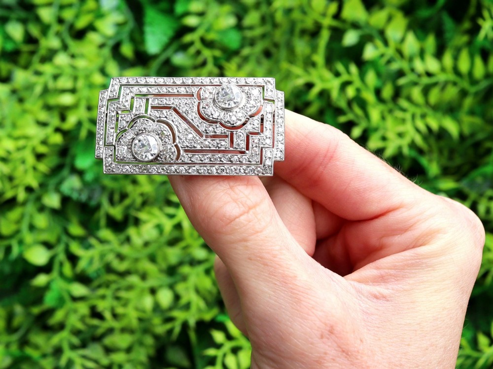 A rectangular Art Deco platinum brooch featuring geometric openwork encrusted with round diamonds and two central bezel-set accent diamonds. View II