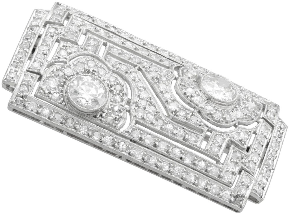A rectangular Art Deco platinum brooch featuring geometric openwork encrusted with round diamonds and two central bezel-set accent diamonds. View VI