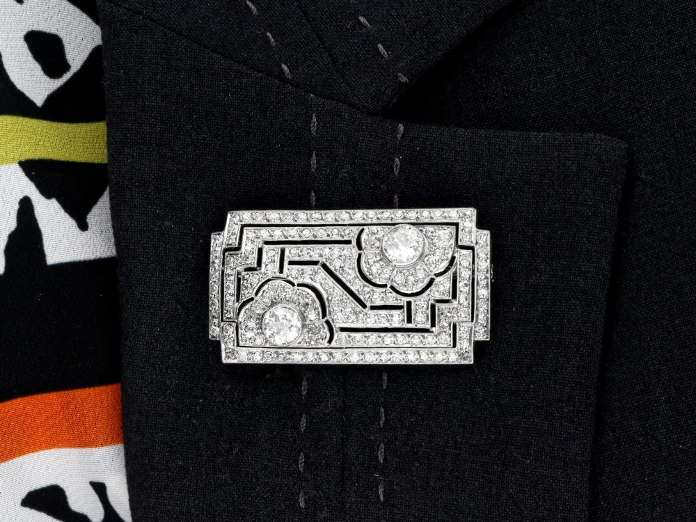 A rectangular Art Deco platinum brooch featuring geometric openwork encrusted with round diamonds and two central bezel-set accent diamonds. View X