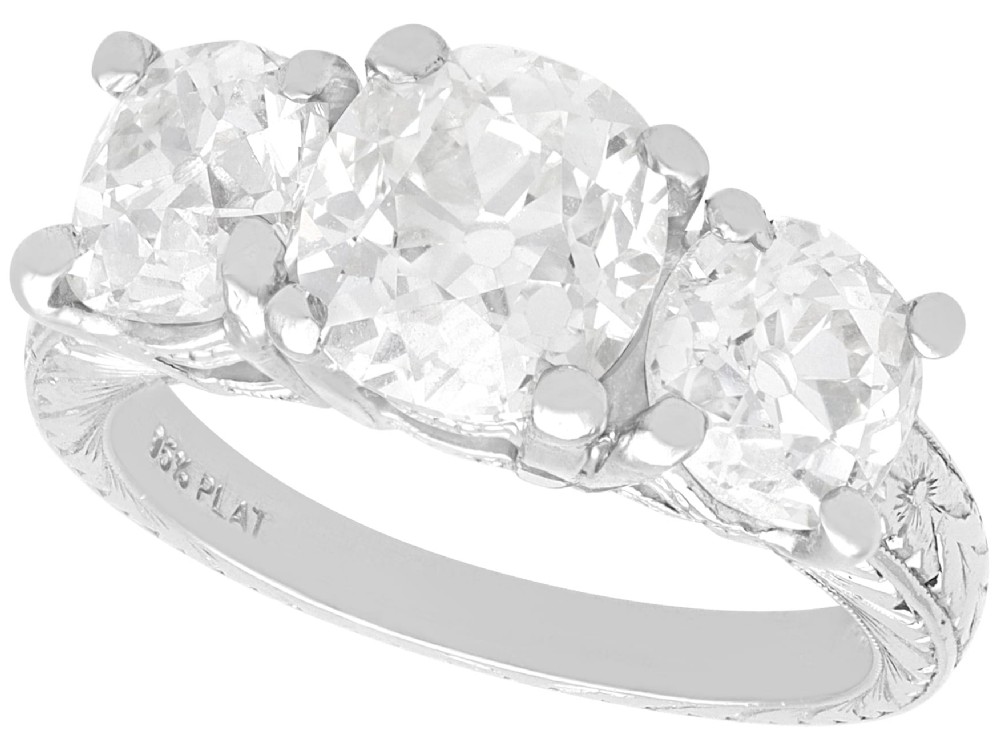 An antique platinum trilogy ring set with three cushion cut diamonds and decorated with hand-engraved shoulders.