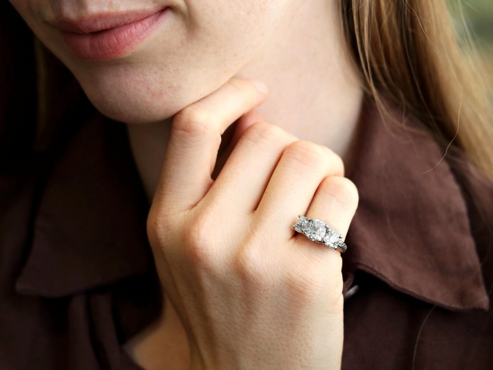 An antique platinum trilogy ring set with three cushion cut diamonds and decorated with hand-engraved shoulders. View IV