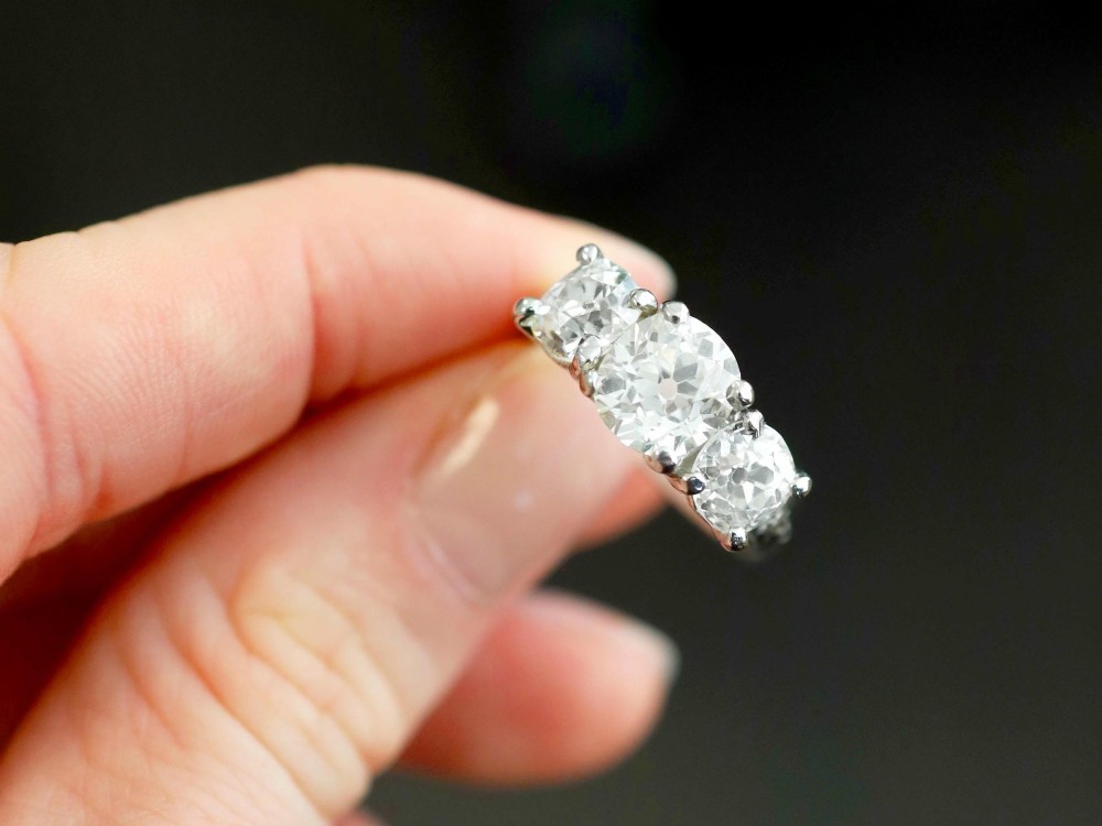 An antique platinum trilogy ring set with three cushion cut diamonds and decorated with hand-engraved shoulders. View V