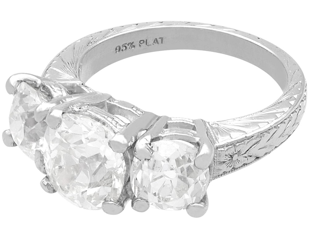 An antique platinum trilogy ring set with three cushion cut diamonds and decorated with hand-engraved shoulders. View VII