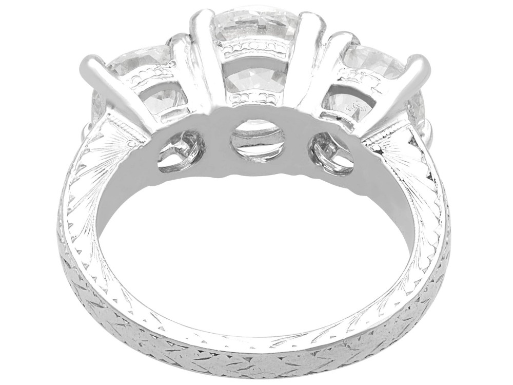 An antique platinum trilogy ring set with three cushion cut diamonds and decorated with hand-engraved shoulders. View VIII