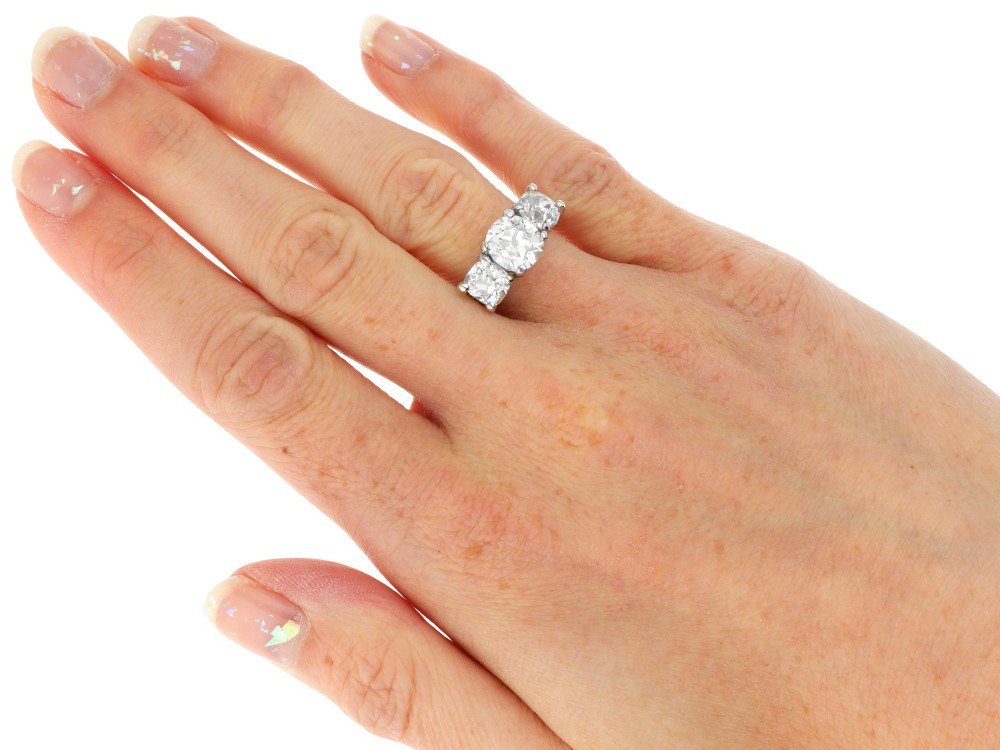 An antique platinum trilogy ring set with three cushion cut diamonds and decorated with hand-engraved shoulders. View X