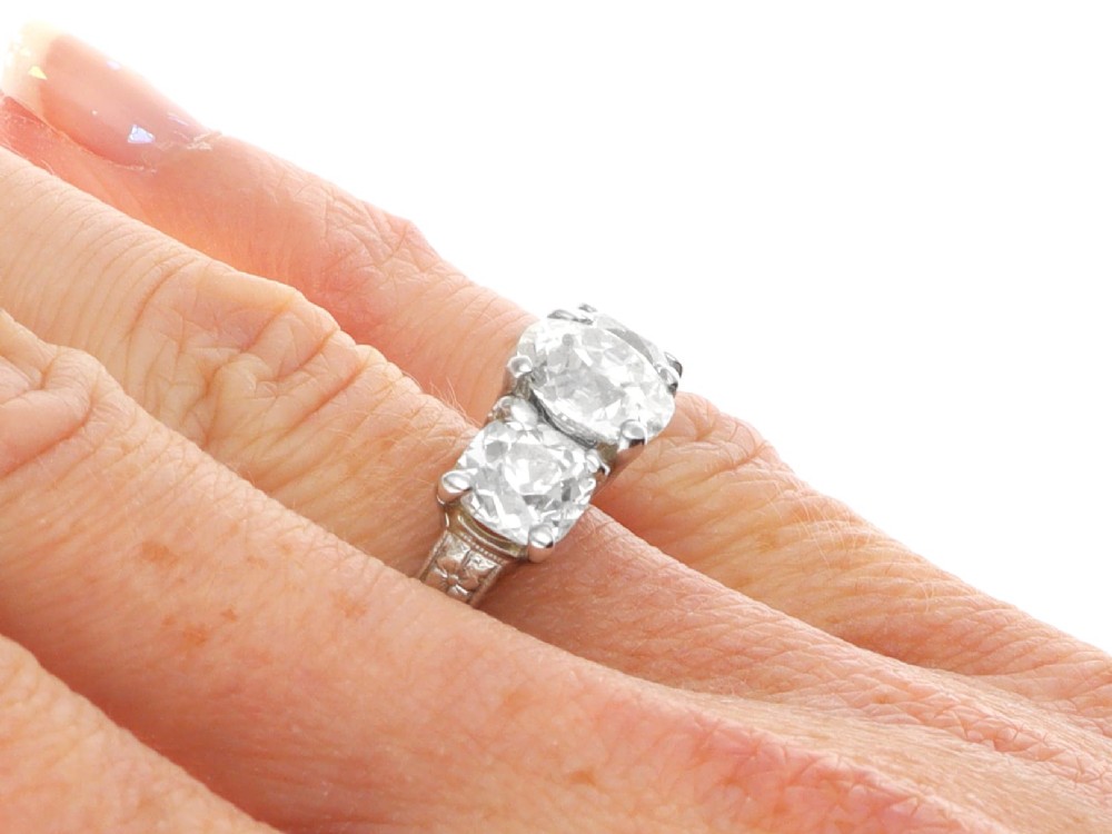 An antique platinum trilogy ring set with three cushion cut diamonds and decorated with hand-engraved shoulders. View XI