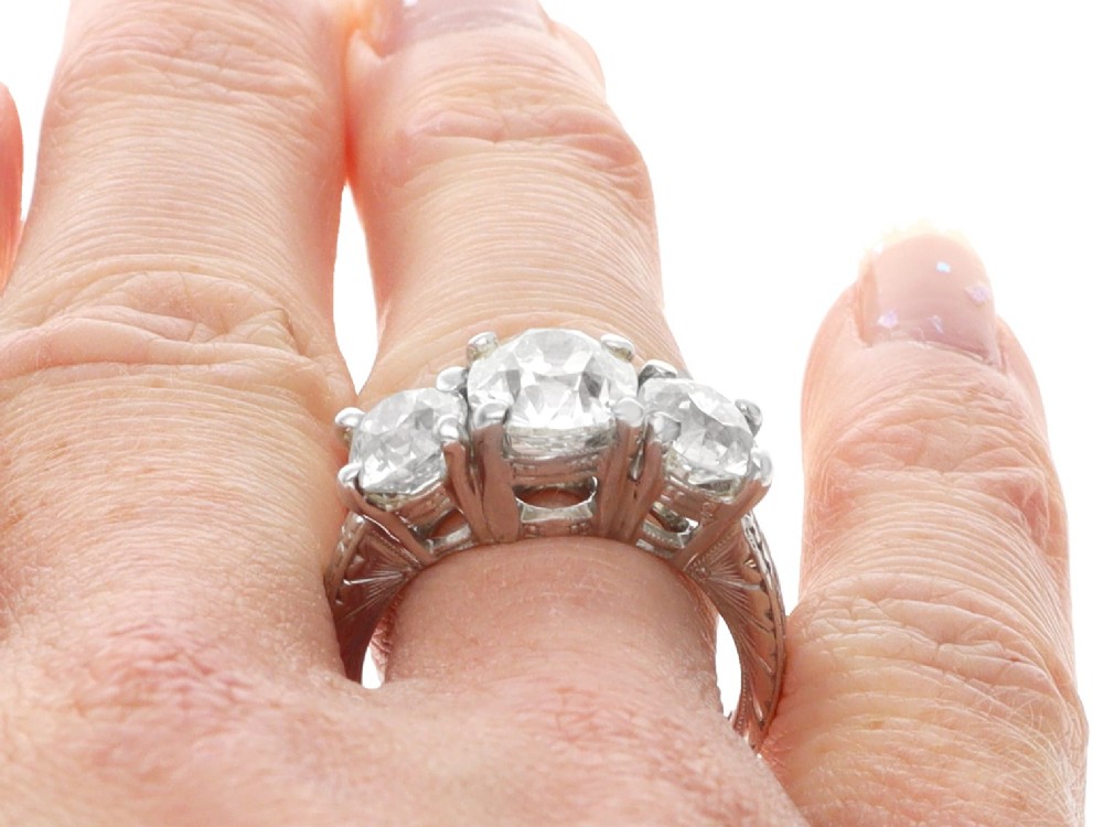 An antique platinum trilogy ring set with three cushion cut diamonds and decorated with hand-engraved shoulders. View XII