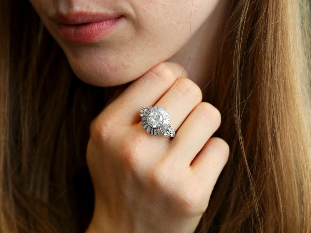 An Art Deco platinum ballerina ring featuring a prominent round central diamond surrounded by a radiating halo of tapered baguette cut diamonds. View V
