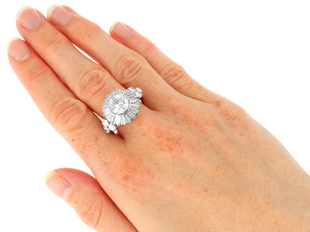 An Art Deco platinum ballerina ring featuring a prominent round central diamond surrounded by a radiating halo of tapered baguette cut diamonds. View IX