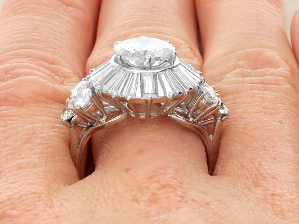 An Art Deco platinum ballerina ring featuring a prominent round central diamond surrounded by a radiating halo of tapered baguette cut diamonds. View XI