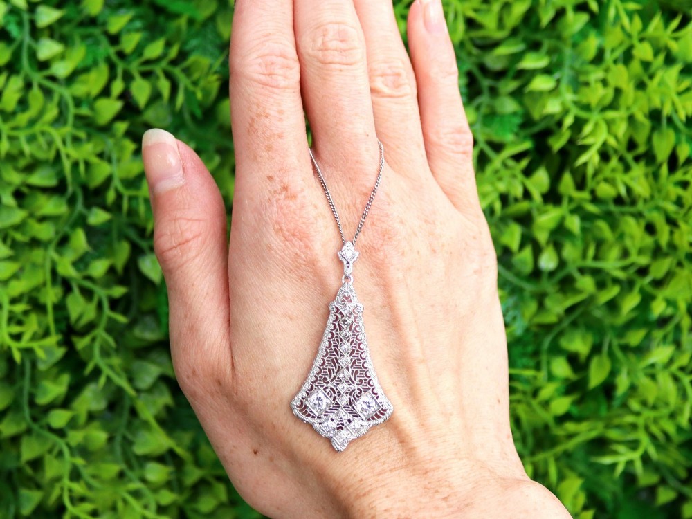 An Art Deco 14ct white gold pendant featuring geometric pierced filigree lattice work set with multiple diamonds suspended from a chain. View II