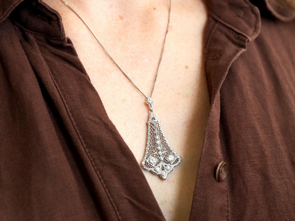 An Art Deco 14ct white gold pendant featuring geometric pierced filigree lattice work set with multiple diamonds suspended from a chain. View III