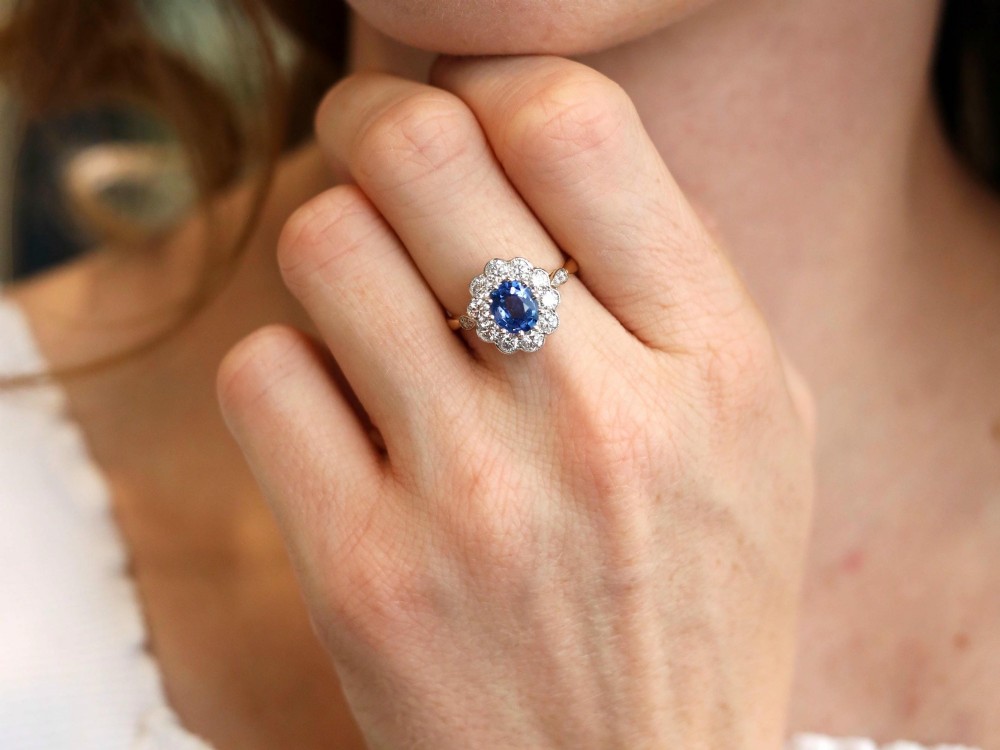 An 18ct yellow gold cluster ring featuring an oval blue sapphire surrounded by a halo of round diamonds set in platinum. View III
