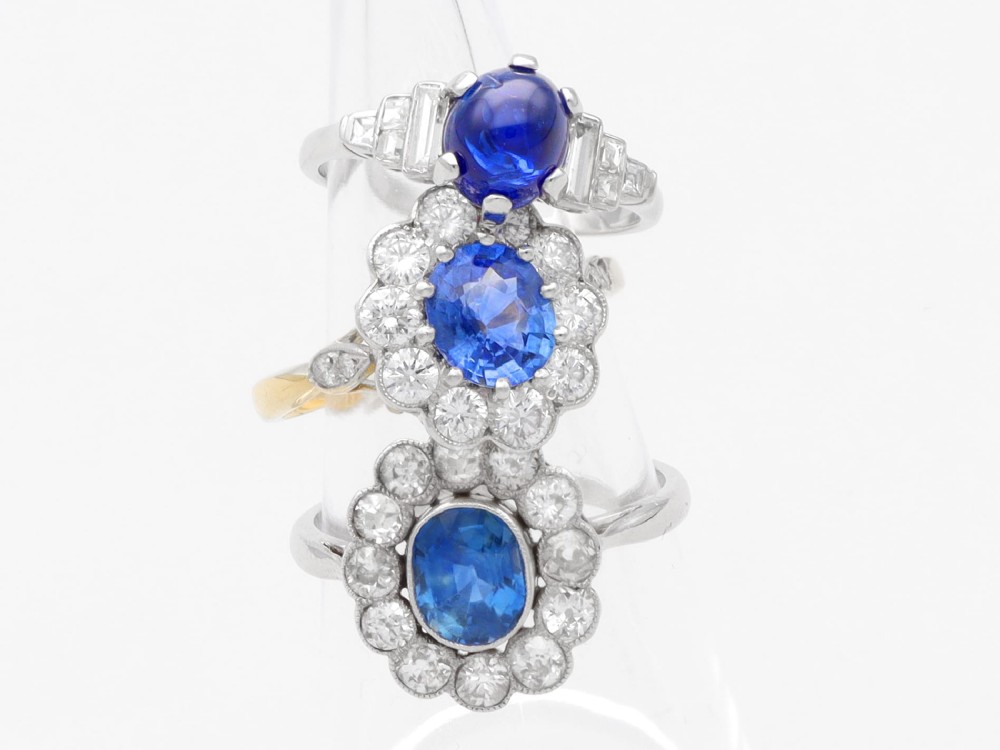 An 18ct yellow gold cluster ring featuring an oval blue sapphire surrounded by a halo of round diamonds set in platinum. View IV
