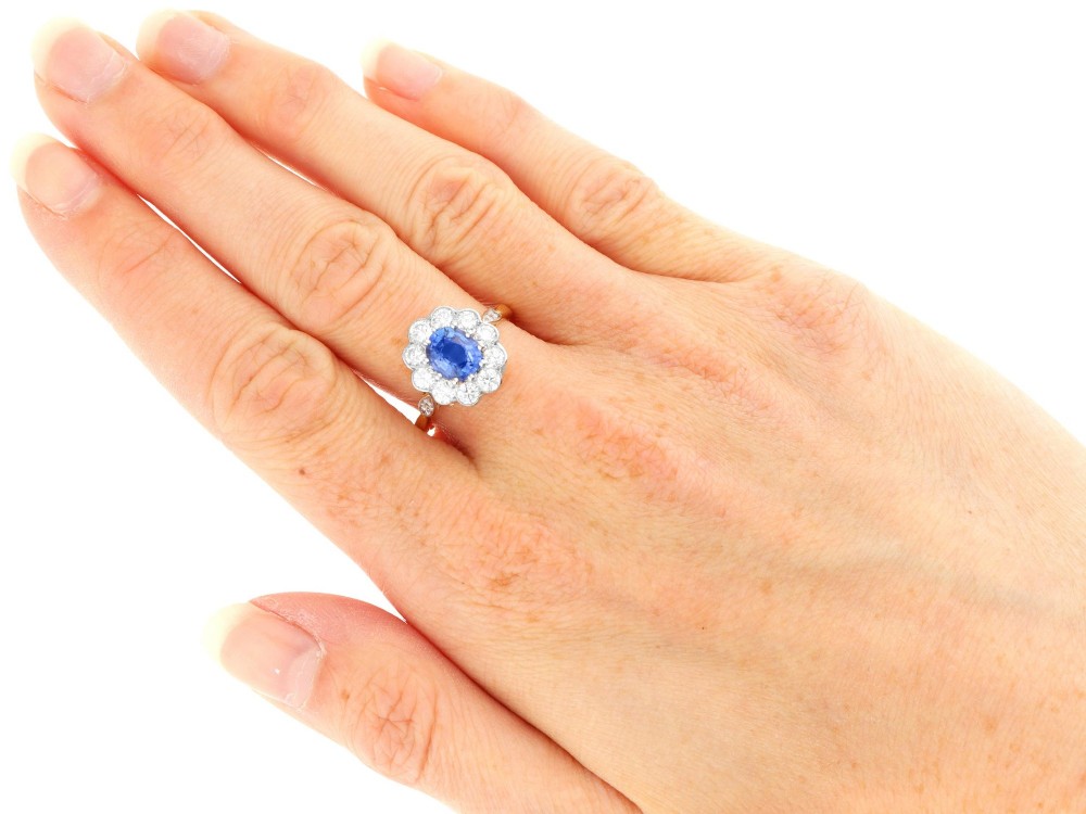 An 18ct yellow gold cluster ring featuring an oval blue sapphire surrounded by a halo of round diamonds set in platinum. View IX