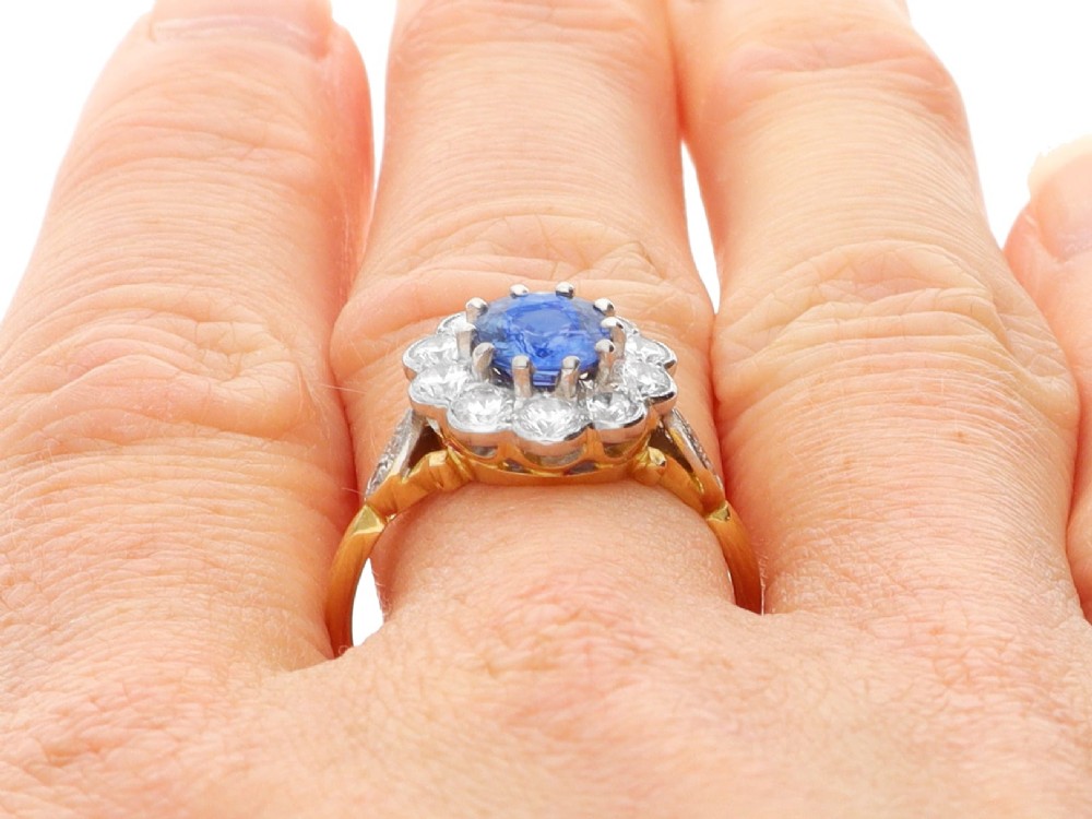 An 18ct yellow gold cluster ring featuring an oval blue sapphire surrounded by a halo of round diamonds set in platinum. View XI