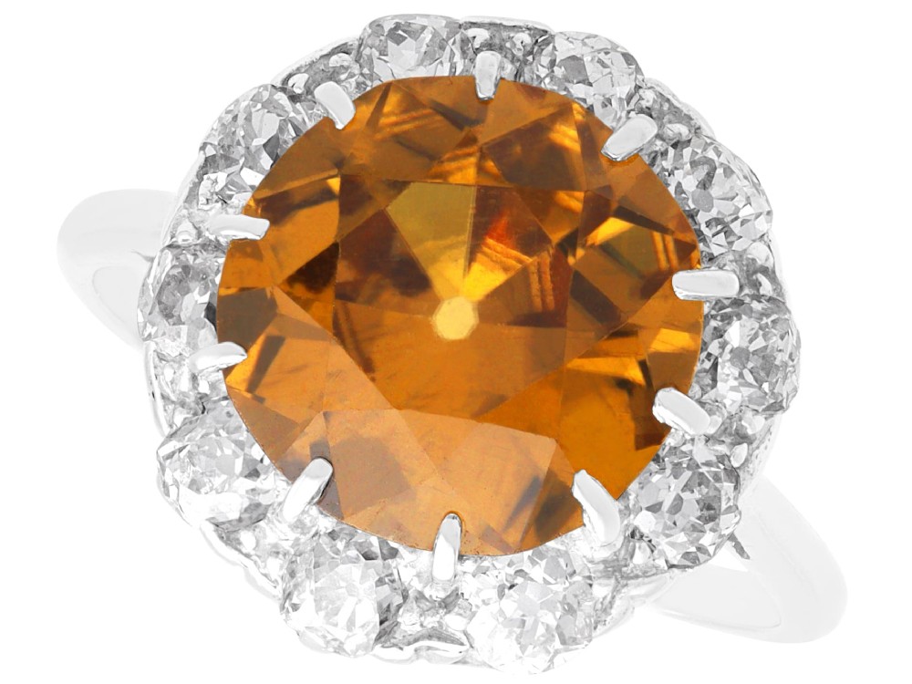 An antique Art Deco platinum ring featuring a central round orange zircon surrounded by a halo of claw-set diamonds.