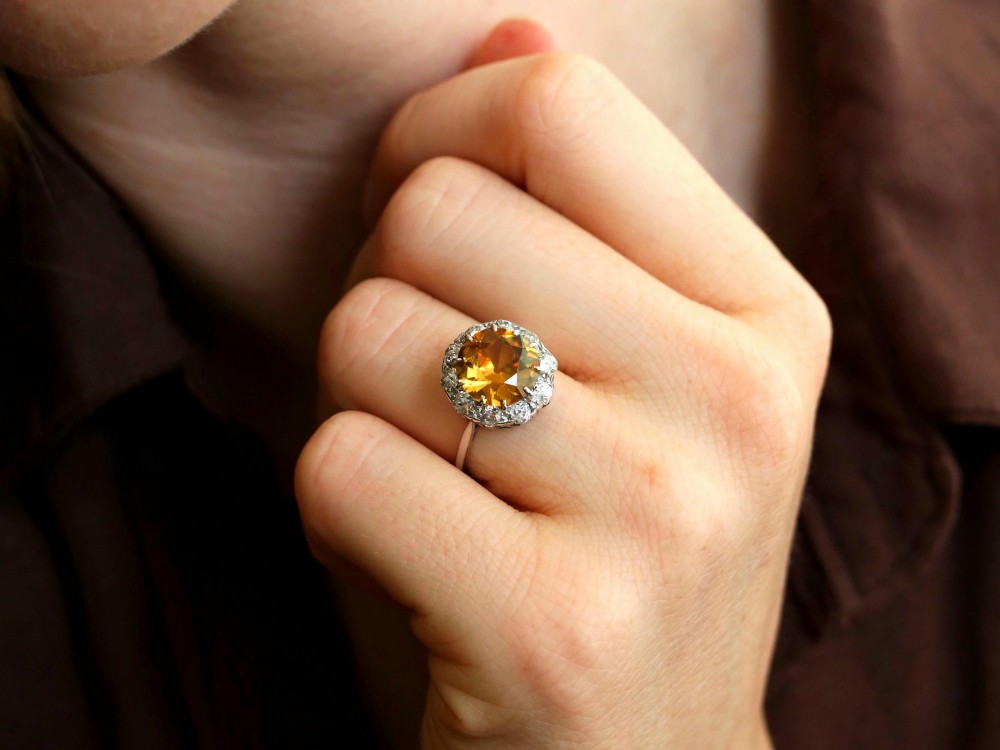 An antique Art Deco platinum ring featuring a central round orange zircon surrounded by a halo of claw-set diamonds. View III