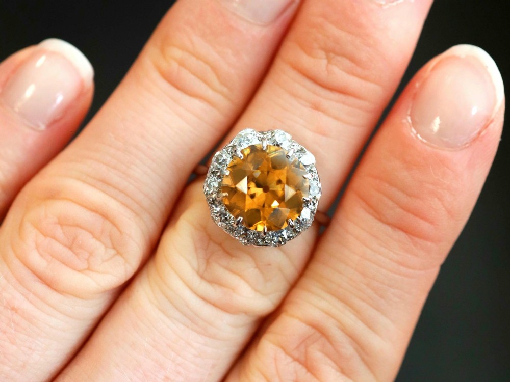 An antique Art Deco platinum ring featuring a central round orange zircon surrounded by a halo of claw-set diamonds. View IV