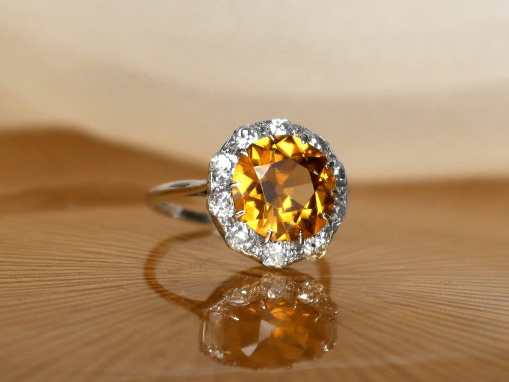 An antique Art Deco platinum ring featuring a central round orange zircon surrounded by a halo of claw-set diamonds. View VII
