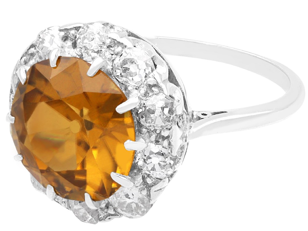An antique Art Deco platinum ring featuring a central round orange zircon surrounded by a halo of claw-set diamonds. View VIII