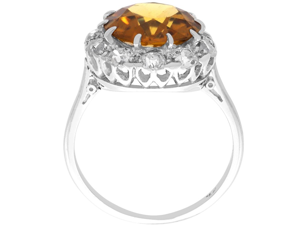 An antique Art Deco platinum ring featuring a central round orange zircon surrounded by a halo of claw-set diamonds. View X