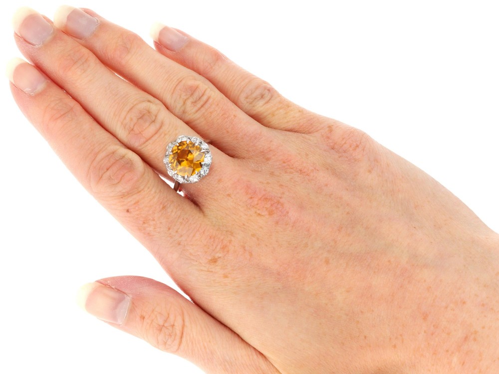 An antique Art Deco platinum ring featuring a central round orange zircon surrounded by a halo of claw-set diamonds. View XII