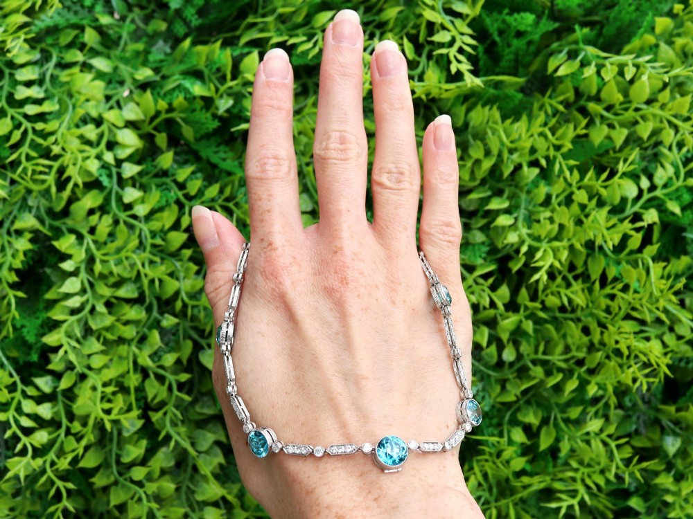 An Art Deco platinum chain necklace featuring five bezel-set round blue zircons separated by geometric diamond-set bar links. View II