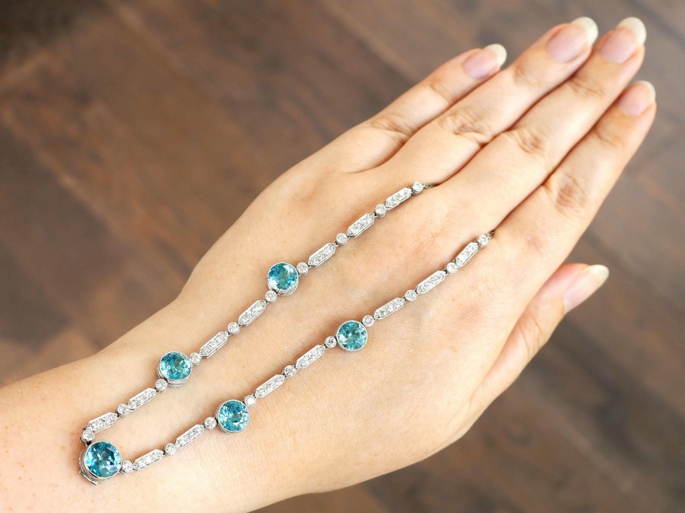 An Art Deco platinum chain necklace featuring five bezel-set round blue zircons separated by geometric diamond-set bar links. View III