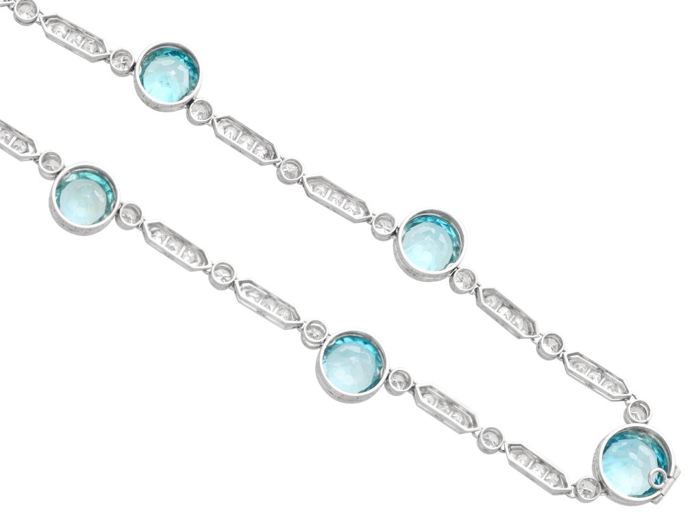 An Art Deco platinum chain necklace featuring five bezel-set round blue zircons separated by geometric diamond-set bar links. View X
