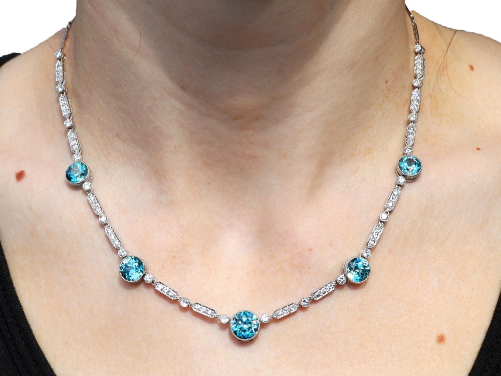 An Art Deco platinum chain necklace featuring five bezel-set round blue zircons separated by geometric diamond-set bar links. View XIII