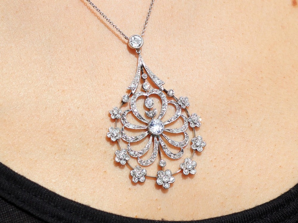 An antique Edwardian openwork platinum pendant set with diamonds in a teardrop silhouette with floral motifs, suspended from a fine chain. View X