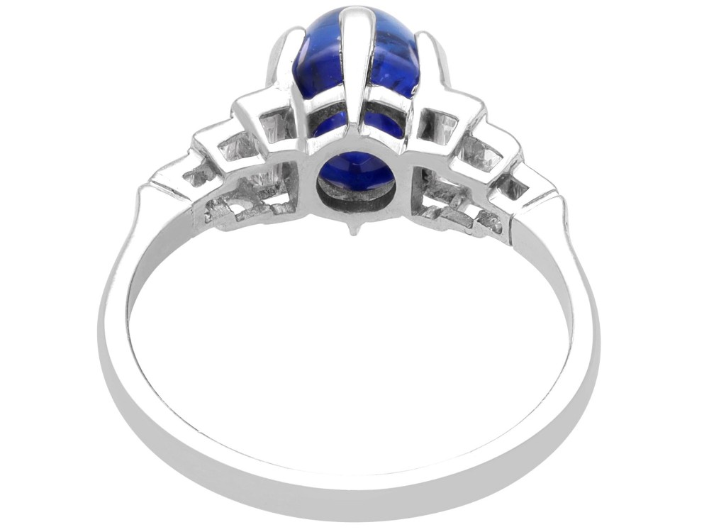 An Art Deco platinum dress ring set with a central oval cabochon blue sapphire flanked by stepped geometric shoulders of baguette cut diamonds. View VII