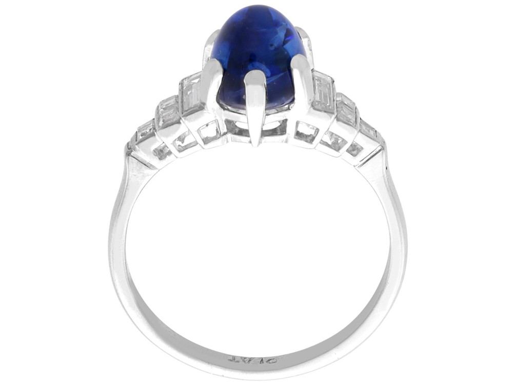 An Art Deco platinum dress ring set with a central oval cabochon blue sapphire flanked by stepped geometric shoulders of baguette cut diamonds. View VIII