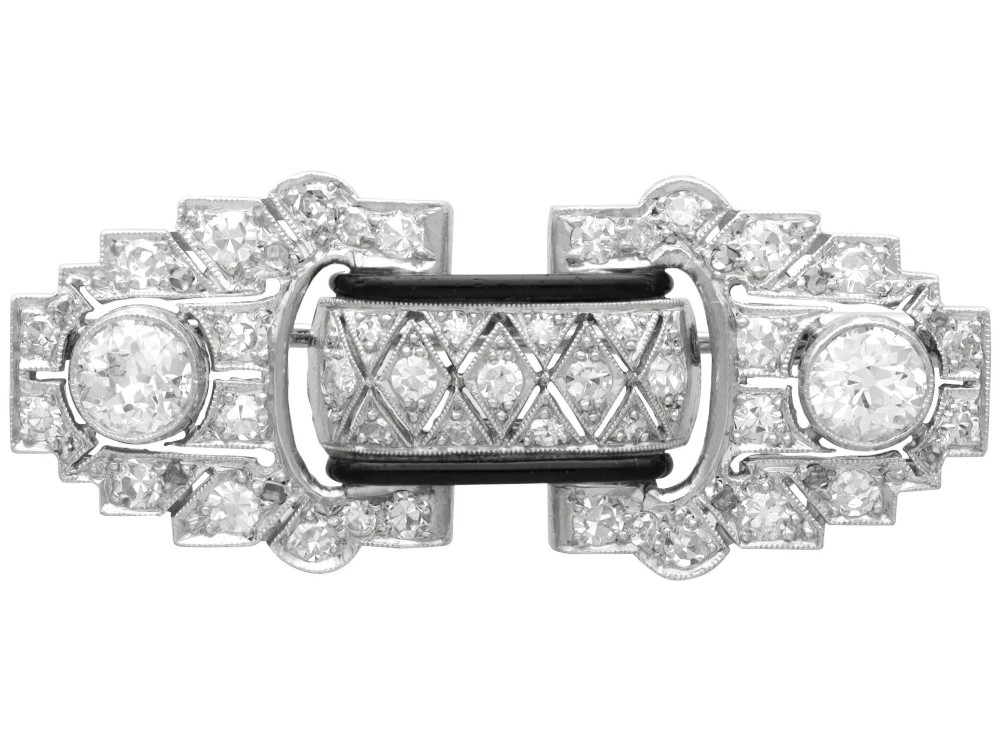 An Art Deco platinum brooch featuring geometric stepped motifs, diamond pave setting, central lattice detail, and black enamel accents.