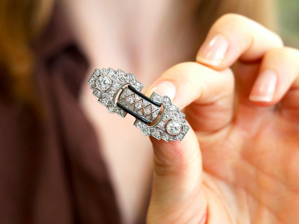 An Art Deco platinum brooch featuring geometric stepped motifs, diamond pave setting, central lattice detail, and black enamel accents. View IV