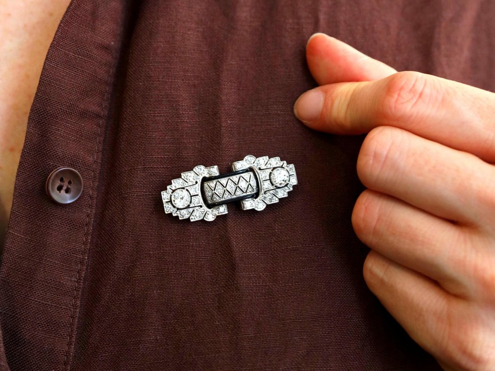 An Art Deco platinum brooch featuring geometric stepped motifs, diamond pave setting, central lattice detail, and black enamel accents. View V