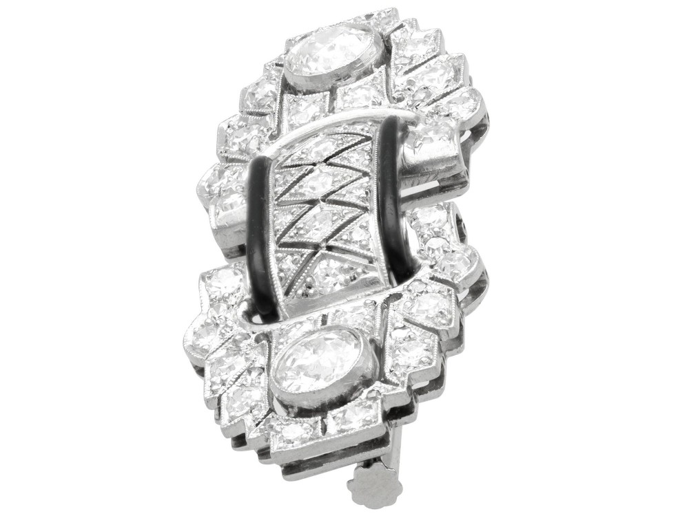 An Art Deco platinum brooch featuring geometric stepped motifs, diamond pave setting, central lattice detail, and black enamel accents. View VII