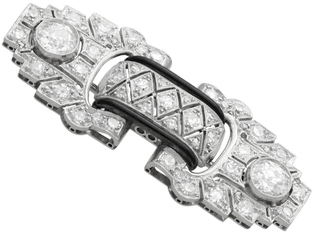 An Art Deco platinum brooch featuring geometric stepped motifs, diamond pave setting, central lattice detail, and black enamel accents. View VIII