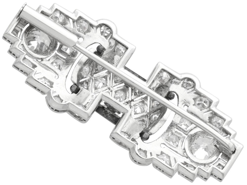 An Art Deco platinum brooch featuring geometric stepped motifs, diamond pave setting, central lattice detail, and black enamel accents. View IX