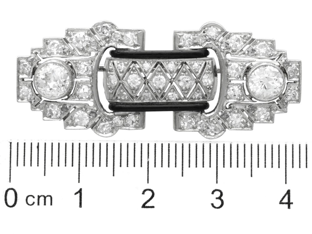 An Art Deco platinum brooch featuring geometric stepped motifs, diamond pave setting, central lattice detail, and black enamel accents. View XI