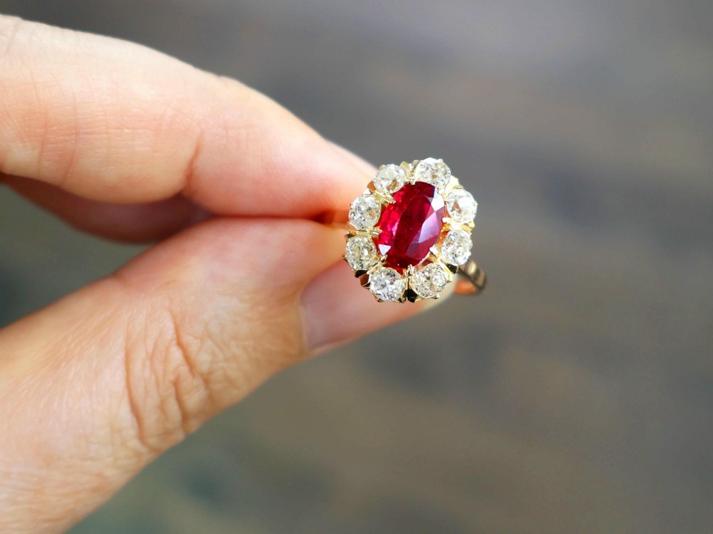An 18ct rose gold cluster ring featuring a central oval red ruby surrounded by eight old cut diamonds set in individual claw settings. View VI