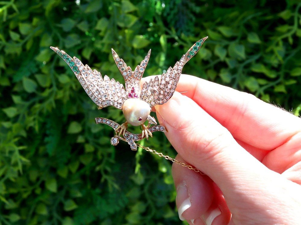 An antique Victorian 18ct yellow gold bird brooch set with diamonds on the wings, emeralds along the outer feathers, a natural pearl body, and ruby details. View II