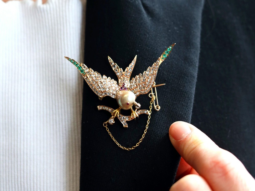 An antique Victorian 18ct yellow gold bird brooch set with diamonds on the wings, emeralds along the outer feathers, a natural pearl body, and ruby details. View III