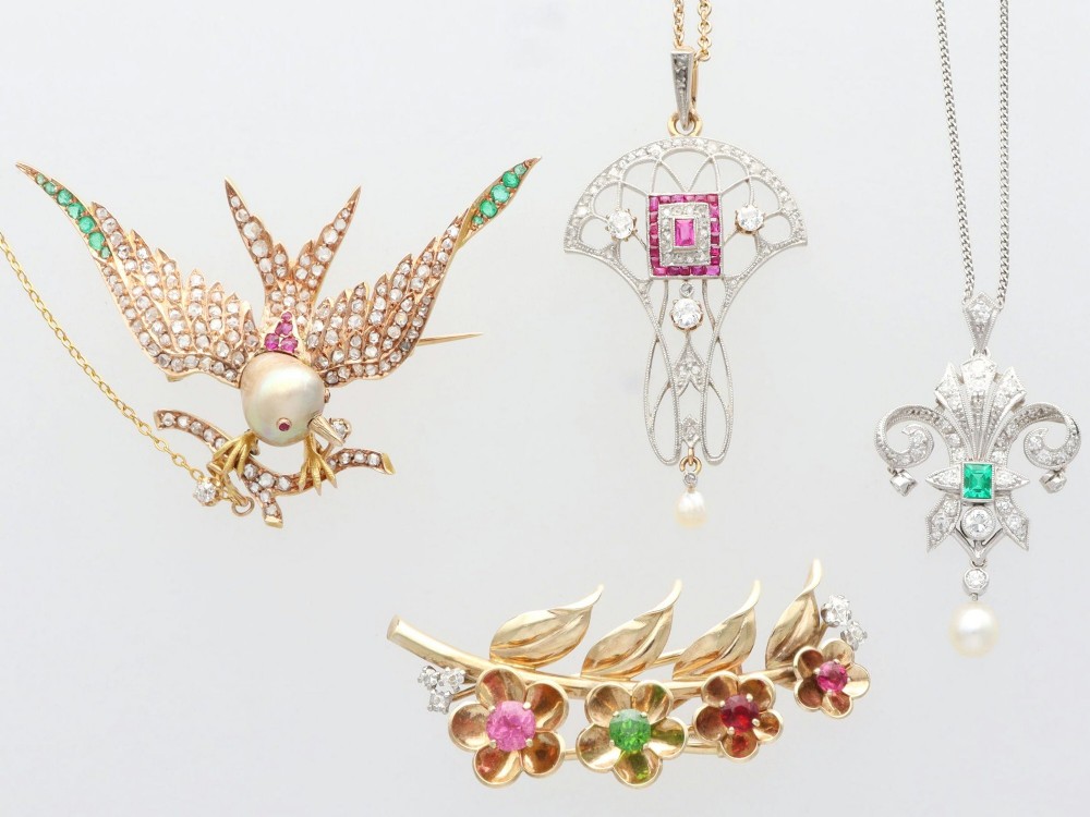 An antique Victorian 18ct yellow gold bird brooch set with diamonds on the wings, emeralds along the outer feathers, a natural pearl body, and ruby details. View V
